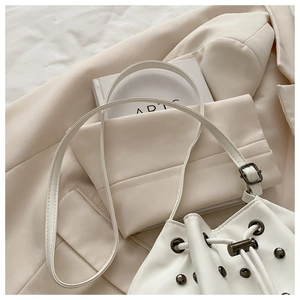 Detail view of white leather drawstring bucket bag with decorative dark metal rivets