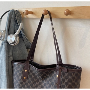 Detail view of large monogram tote bag with brown leather trim and metallic rivets