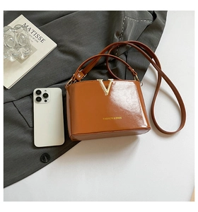Detailed shot of brown glossy leather bag with gold V-buckle and matching slim shoulder strap