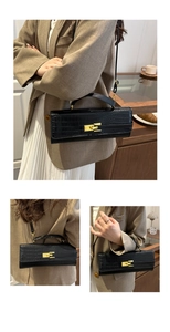 Detail of black crocodile pattern baguette bag with golden metal lock and strap