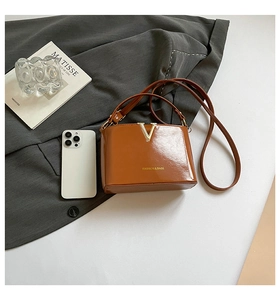 Detail of caramel glossy leather bag with metal V-buckle and elegant thin shoulder strap