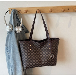 Detail of coffee tote bag with M letter pattern, thin straps and metal logo charm
