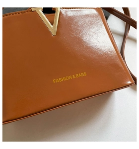 Detail of glossy brown patent leather bag with gold V-buckle and fashion branding