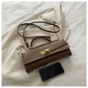 Close-up of brown crocodile embossed baguette bag with gold metal buckle on beige fabric