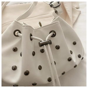 Detail of white drawstring bucket bag featuring metallic rivets and leather texture