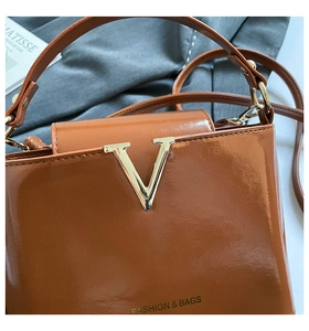 Detailed shot of brown glossy leather bag with gold V-buckle and fashion branding
