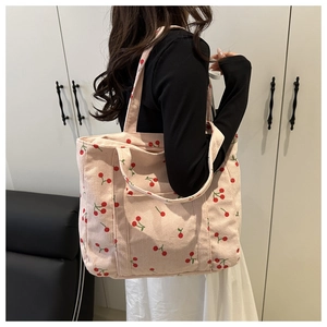 Vue latérale du sac fourre-tout en velours côtelé à motif cerise porté sur l'épaule