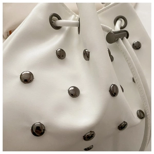 Close-up of white leather bucket bag with dark grey metal rivets and drawstring details