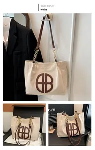 Detalle del bolso tote de lona blanca con logo de cuero marrón y cadena metálica dorada