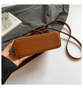 Detail view of the rounded rectangular base and fine stitching of this brown glossy bag