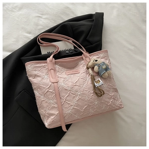 Detail of pink embroidered tote bag with plush bear charm on black suit jacket background