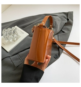 Detail of a caramel brown glossy patent leather mini handbag with a structured square design