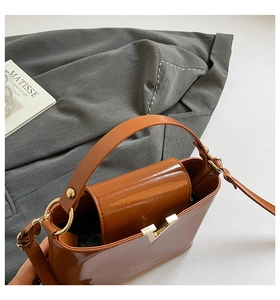 Detail of a brown patent leather bucket bag with a gold V-shaped buckle and metal hardware