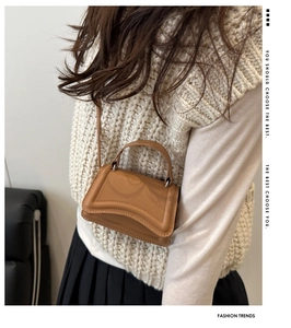 Model wearing a caramel leather crossbody square bag with a curved flap and slim strap