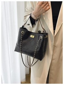 Detail of black quilted bucket bag with gold twist lock and chain strap on a trench coat