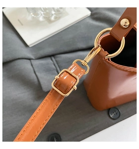 Detail of the glossy brown shoulder bag showing gold metal rings and adjustable strap