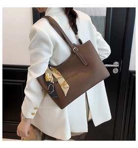 Detail of dark brown tote bag with decorative silk scarf on a model wearing a white suit