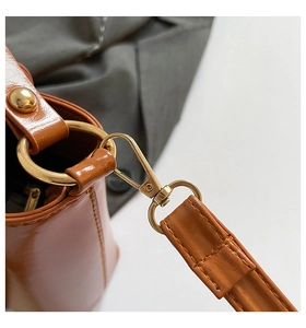 Detail of glossy brown leather bag featuring golden metal rings and detachable strap hooks