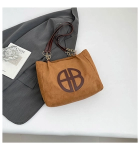 Détail d'un sac cabas en daim marron avec logo en cuir et chaînes métalliques dorées