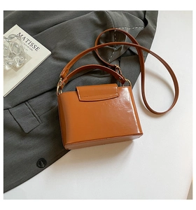 Detail of glossy caramel leather handbag on grey blazer with artistic props