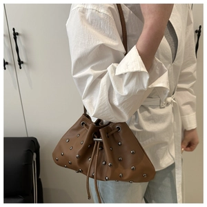 Detail of brown bucket bag featuring silver rivets and adjustable drawstring closure
