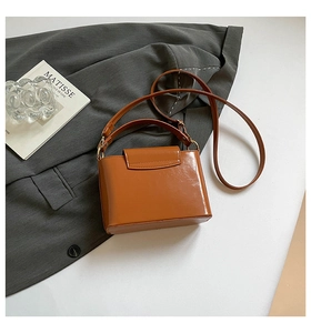 Detail of a shiny brown leather crossbody bag with gold hardware and top handle