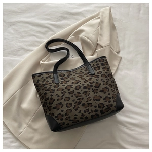 Detail of leopard print tote bag with black leather straps on a beige blazer background
