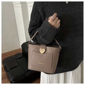 Detailed close-up of taupe bucket bag featuring gold heart buckle and leather texture