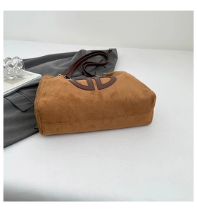 Détail d'un cabas en daim marron avec patch logo en cuir et longue bandoulière réglable