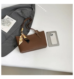 Detailed close-up of brown leather tote bag with white stitching and decorative silk scarf