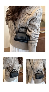 Detail of a black mini crossbody bag with unique wavy textured edge and matte finish