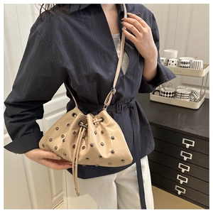 Detailed view of beige drawstring bucket bag with metal rivets worn by a model