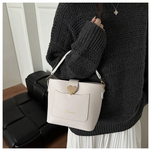 Détail du sac seau crème montrant la boucle cœur dorée et l'inscription sur la poche