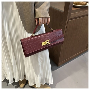 Close-up of wine red baguette bag with crocodile texture and gold clasp on model