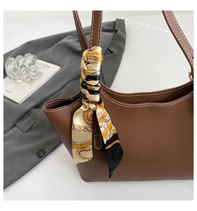 Detail of brown leather tote bag featuring white contrast stitching and printed silk scarf
