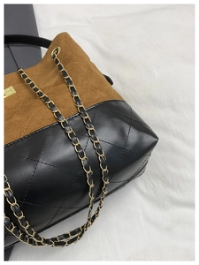 Close-up of contrast stitching, brown suede, and black quilted leather with chain strap