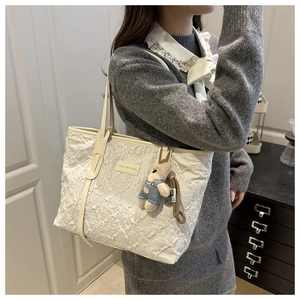 Detailed embroidery on a white tote bag with a cute bear charm and leather handle
