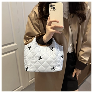 Detail of white quilted handbag featuring black bow embroidery and brown leather trim accents