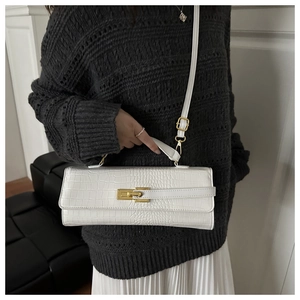 Detail of white crocodile embossed baguette bag with golden clasp on a model shoulder