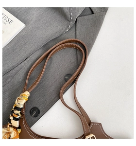 Detail of brown leather tote strap with contrast stitching and floral silk scarf accent