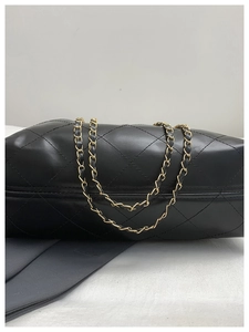 Detail of classic black quilted leather texture and woven chain strap on shoulder bag