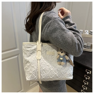 Detail of white textured tote bag with leather strap and cute bear plush charm accessory