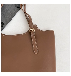 Detail of brown leather tote bag showing white contrast stitching and gold buckle strap