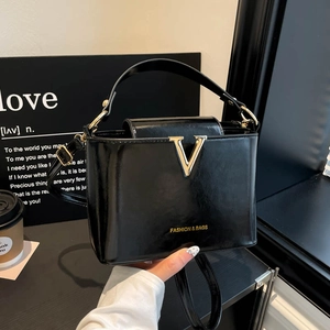 Elegant black patent leather handbag with gold V-buckle and versatile shoulder strap