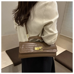 Detail of a brown crocodile pattern leather baguette bag with a gold metal twist lock