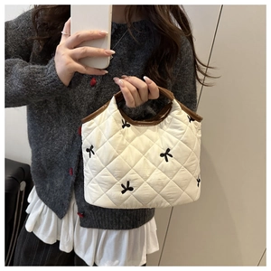 Detail of white quilted bag with black bow embroidery and brown leather handles