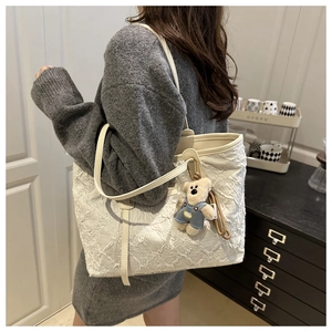 Detail of white embossed floral tote bag with cute bear charm worn over the shoulder