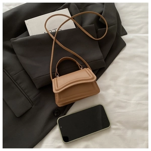 Detail of mini tan crossbody bag with decorative stitching on a blazer background