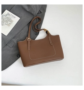 Detail of a brown tote bag featuring white stitching and a patterned silk scarf on the handle