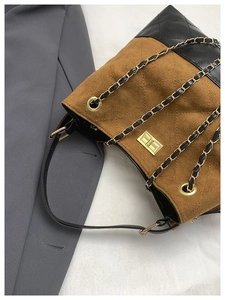 Detail of color-block brown suede bucket bag with quilted patterns and gold metal lock